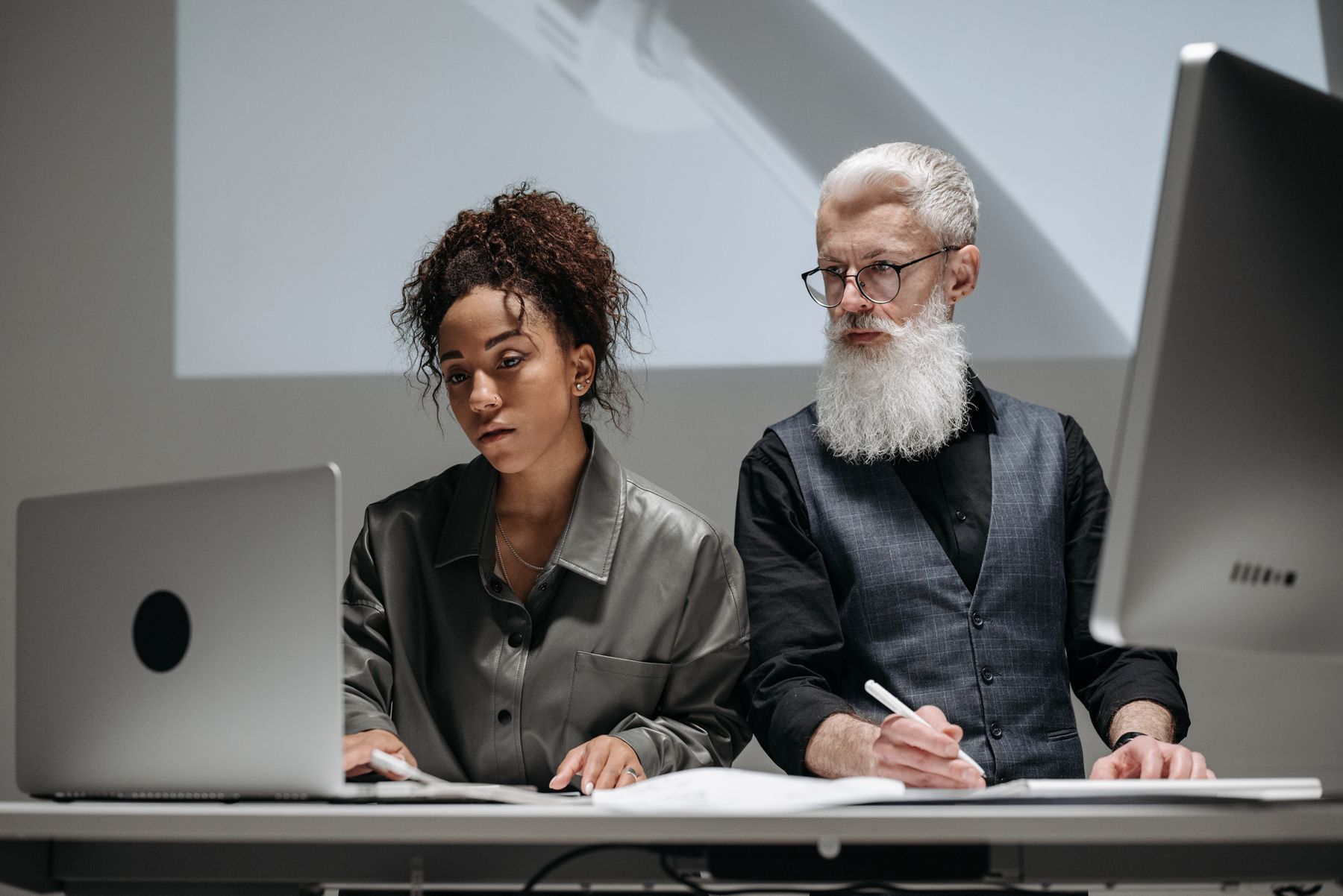 Two professionals reviewing laptops and a written project brief.