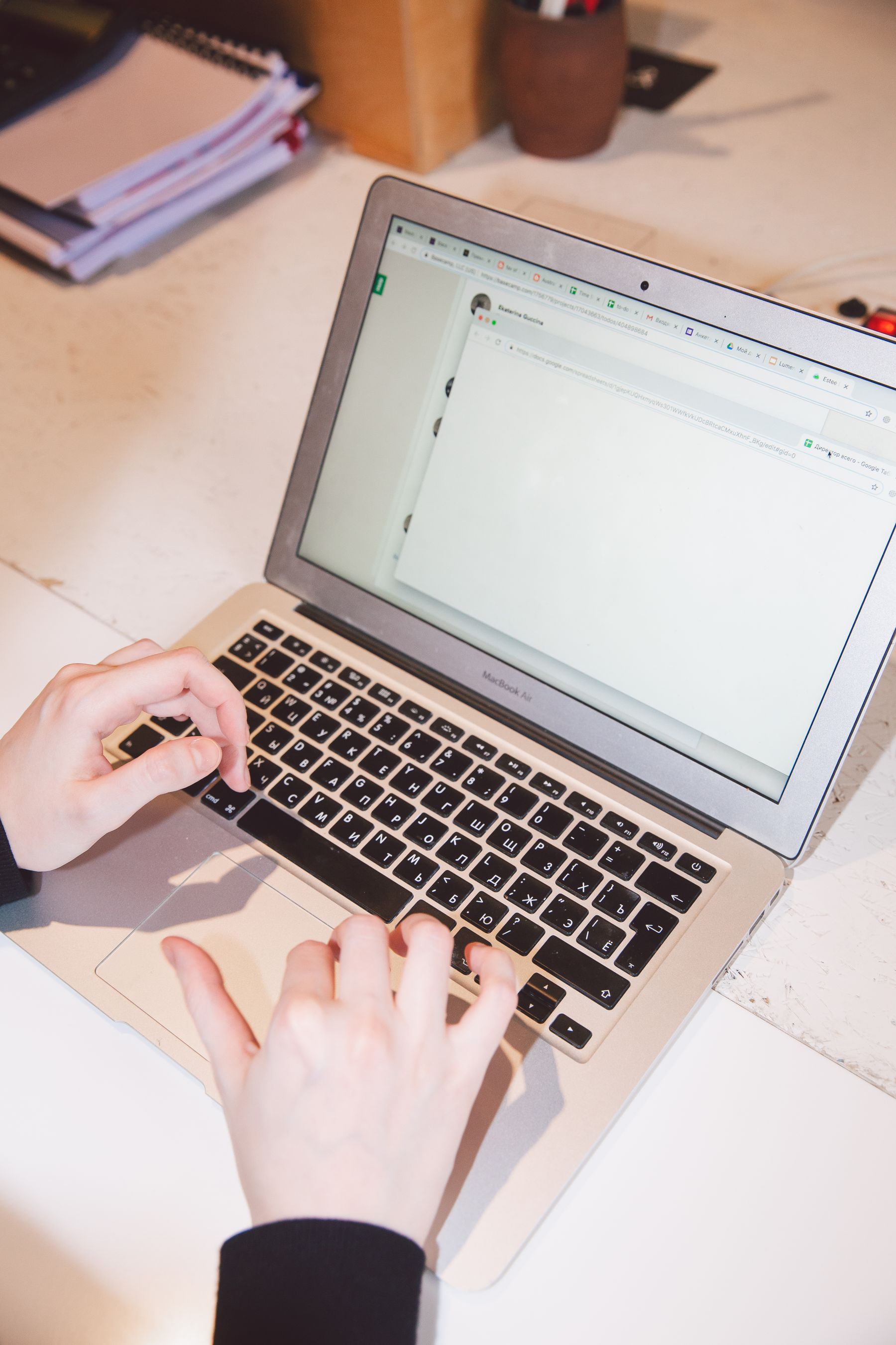 Hands using a laptop at a desk with notebooks and a plant.