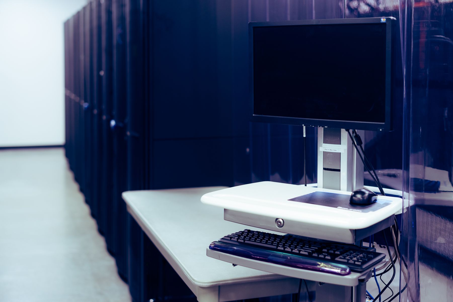 A computer workstation positioned beside server racks.