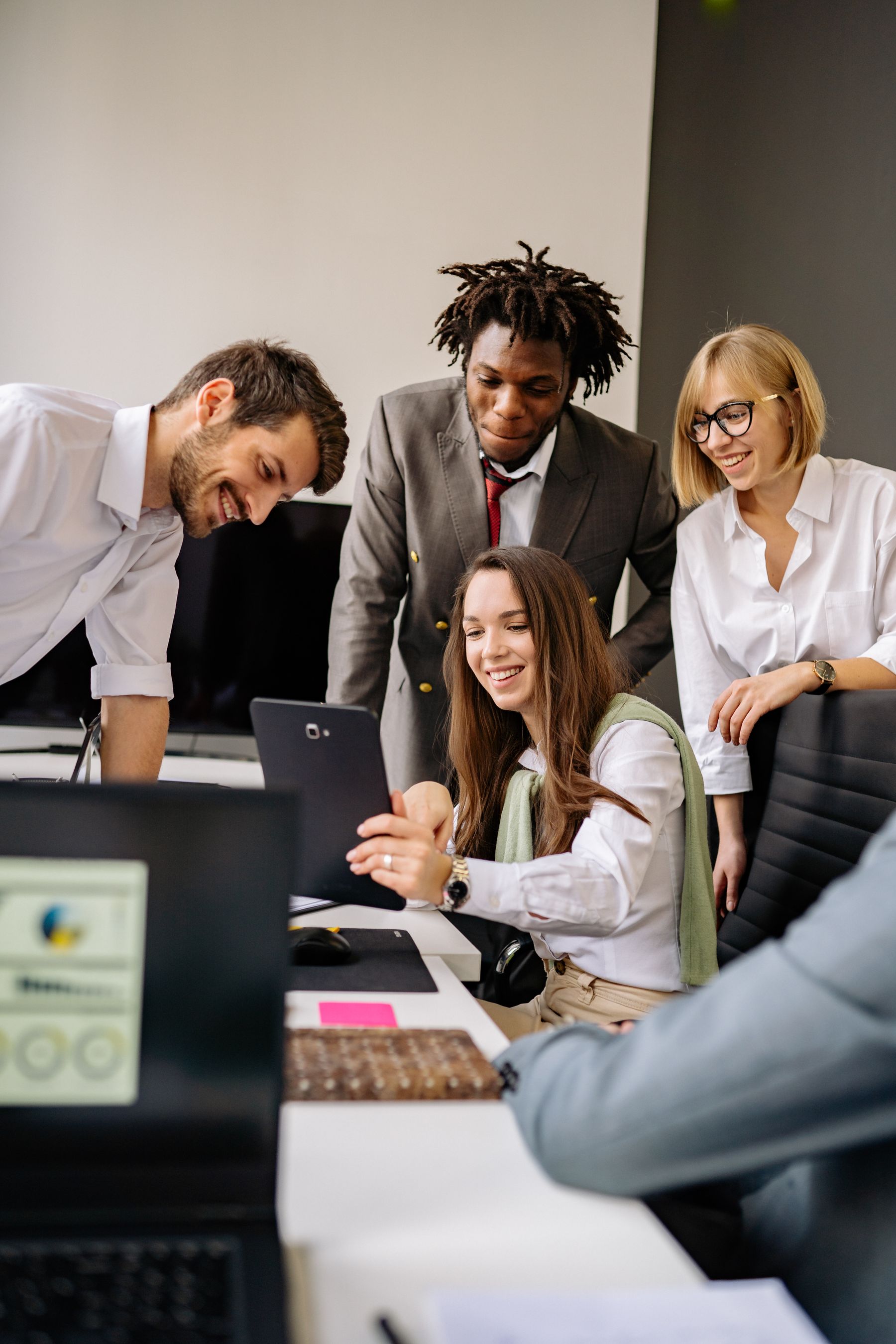 A group reviewing a tablet and computer screens around a working desk.