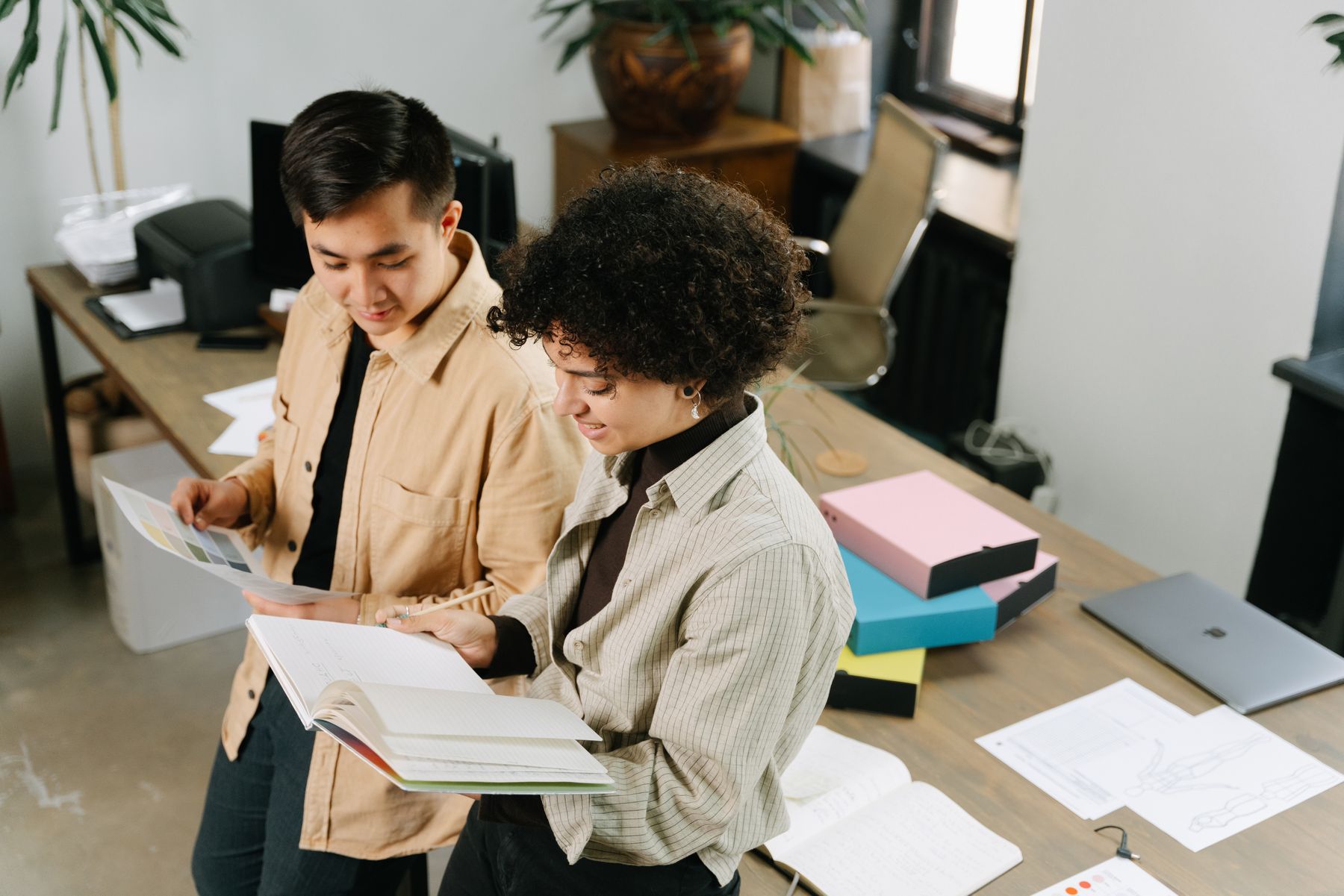 Two professionals reviewing a colour guide and written brief in a workspace.