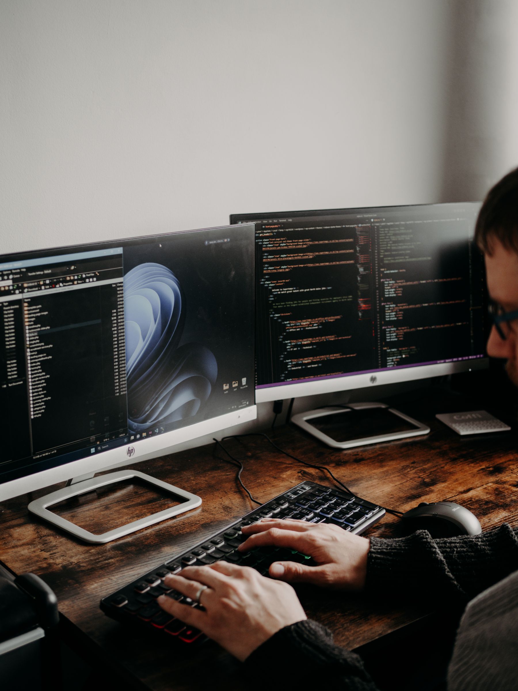 A developer working at two monitors displaying website code.