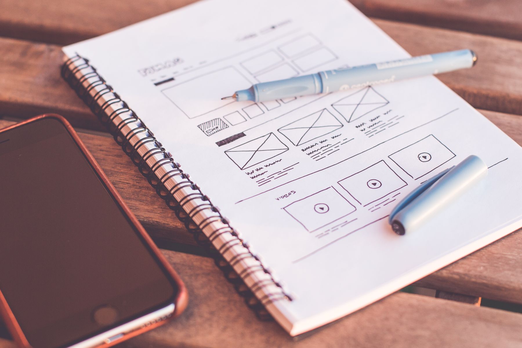 Hand-drawn website wireframes in a notebook beside a phone and pen.
