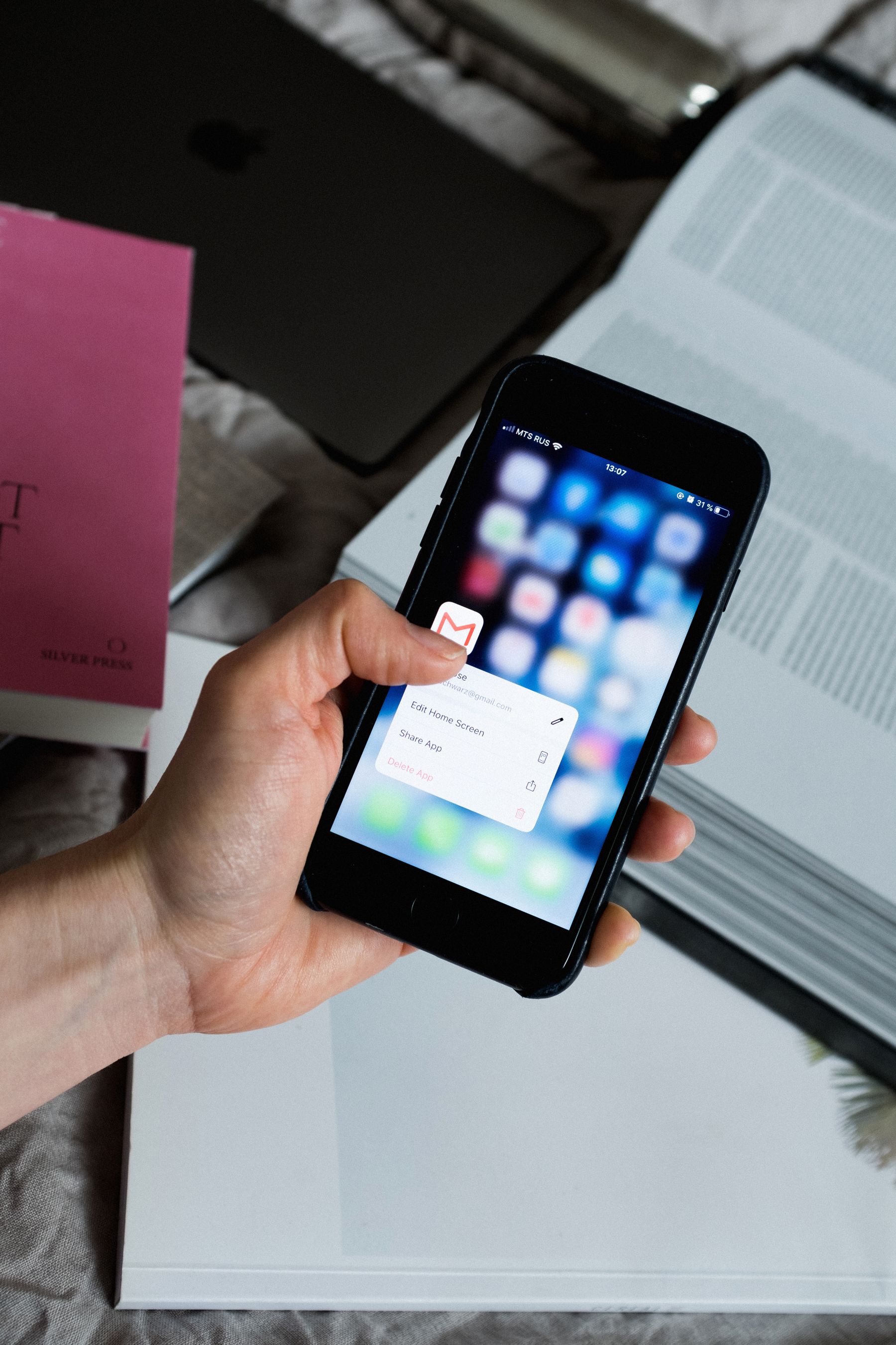 A hand holding a smartphone with an email app beside notebooks.