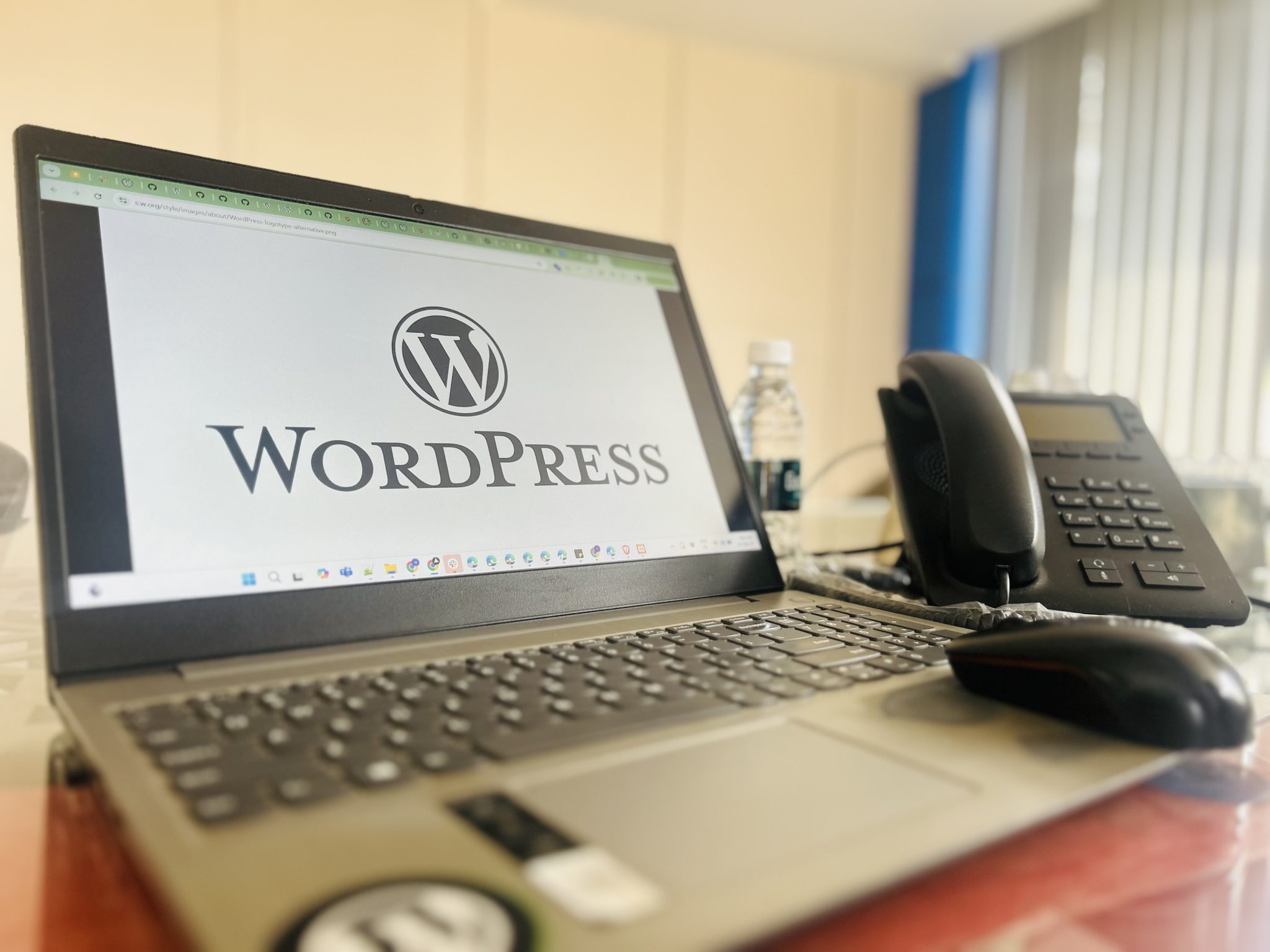 A laptop displaying the WordPress logo beside a desk phone.